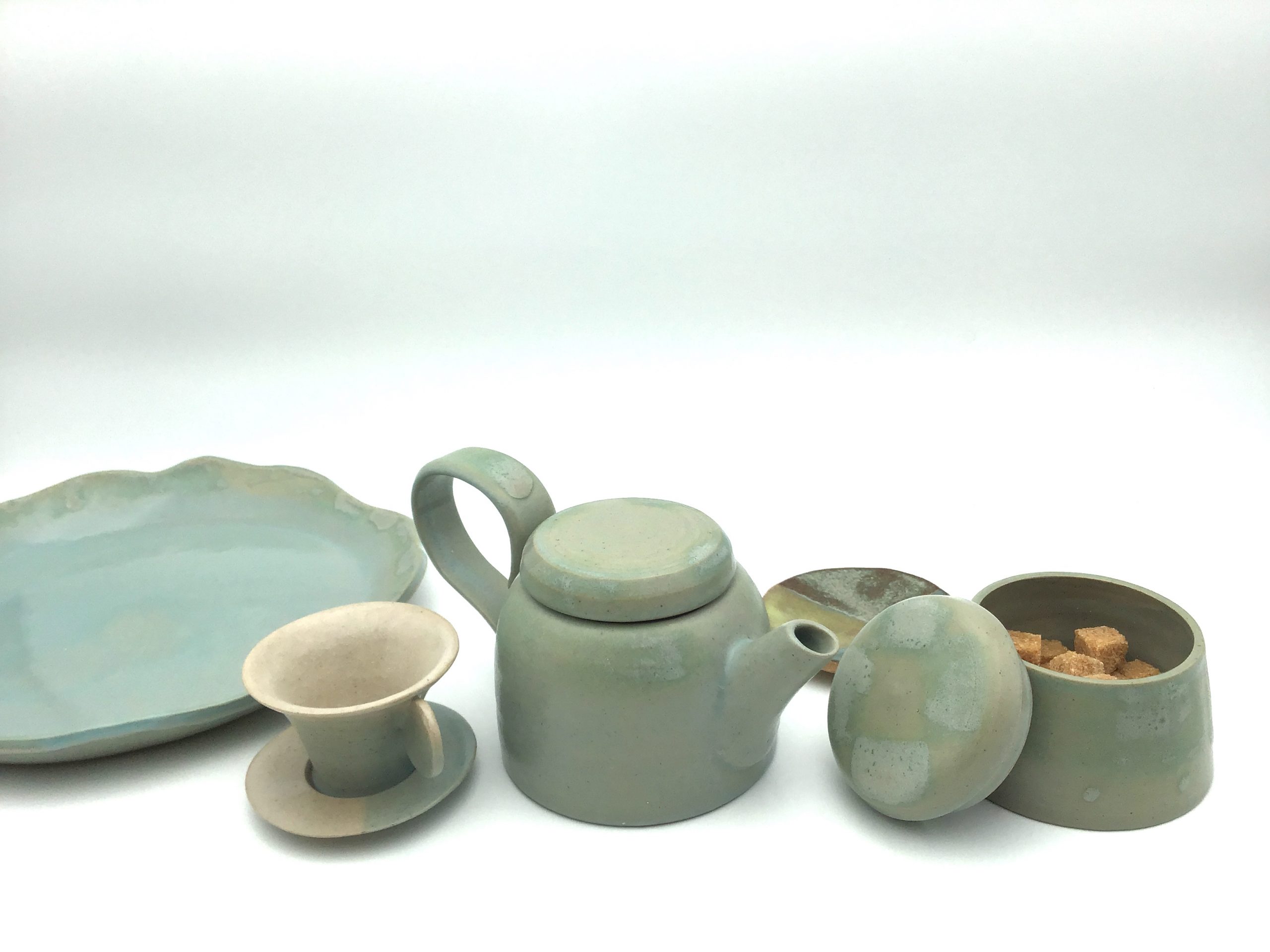 Céramiques artisanales, de couleur bleu pale : théière, tasse et pot à sucre.